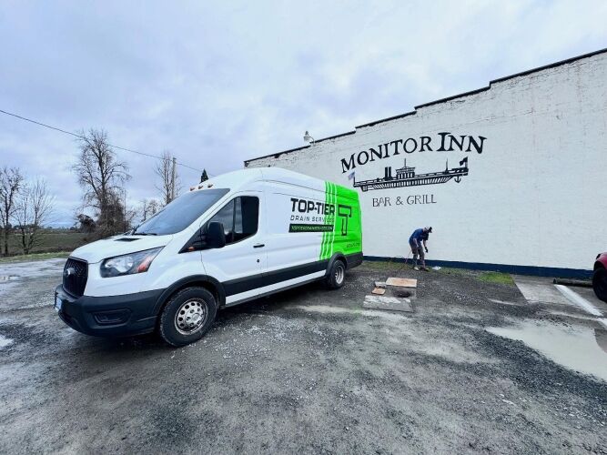 A white and green Top Tier Drain and Sewer van is parked outside Monitor Inn Bar & Grill, with a person working near the building’s wall.
