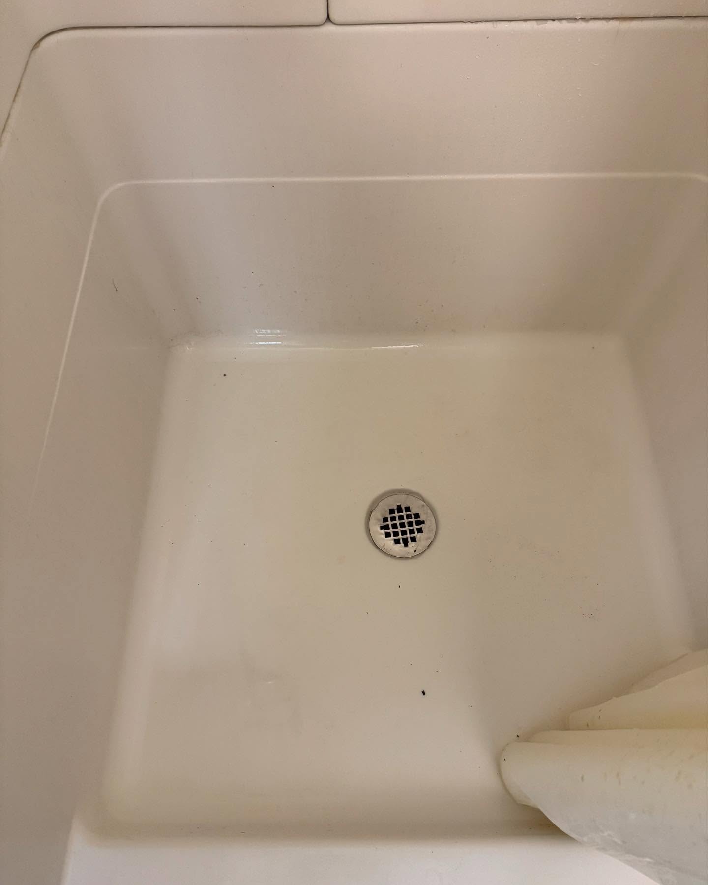 A white shower or bathtub with a small drain in the center and a curtain partially visible in the lower right corner.