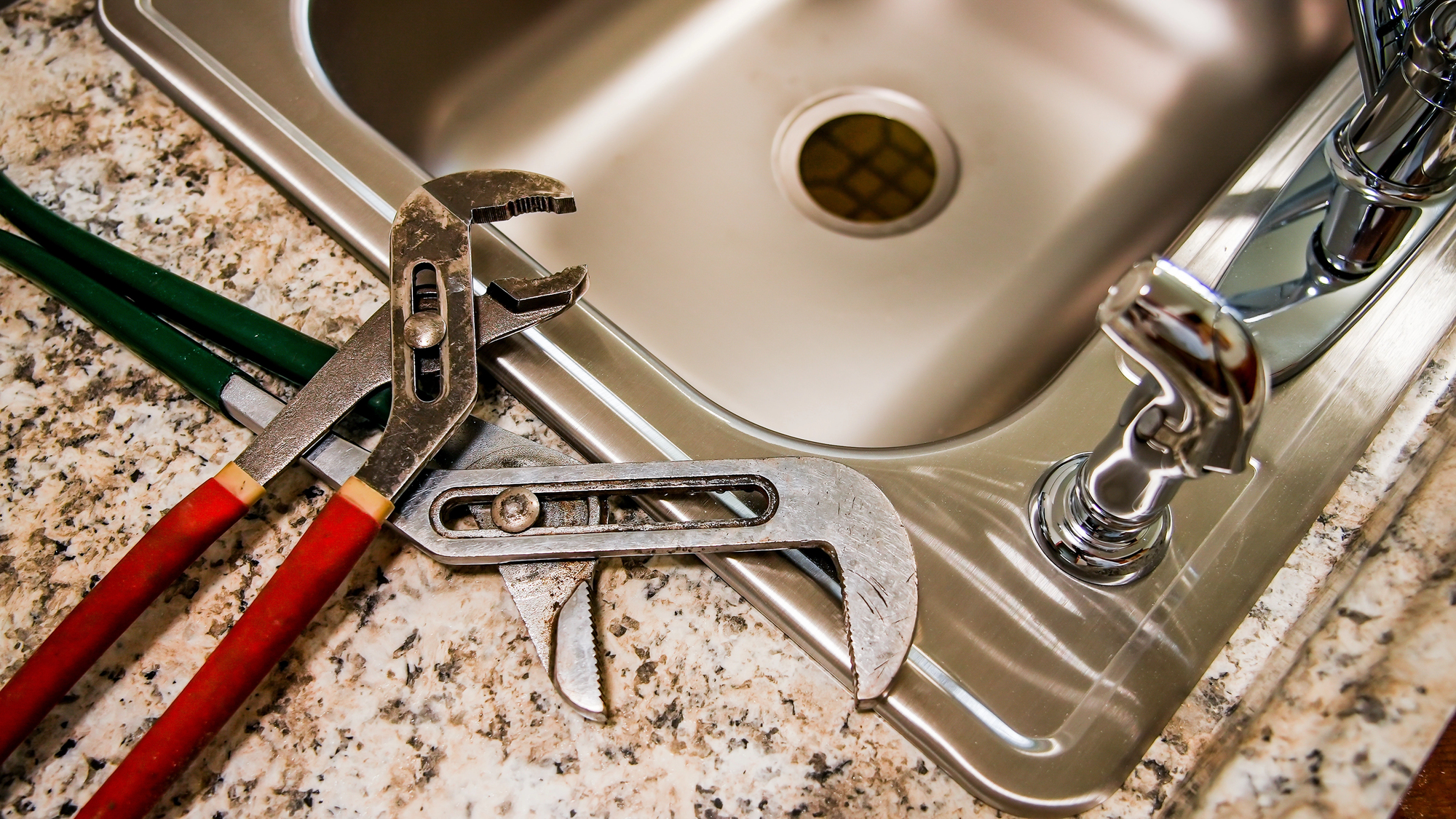 Two wrenches lie next to a stainless steel sink and faucet on a granite countertop.